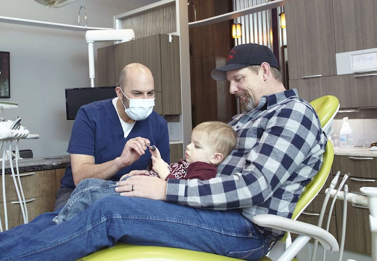 dad with his toddler sitting on his lap at the dentist
